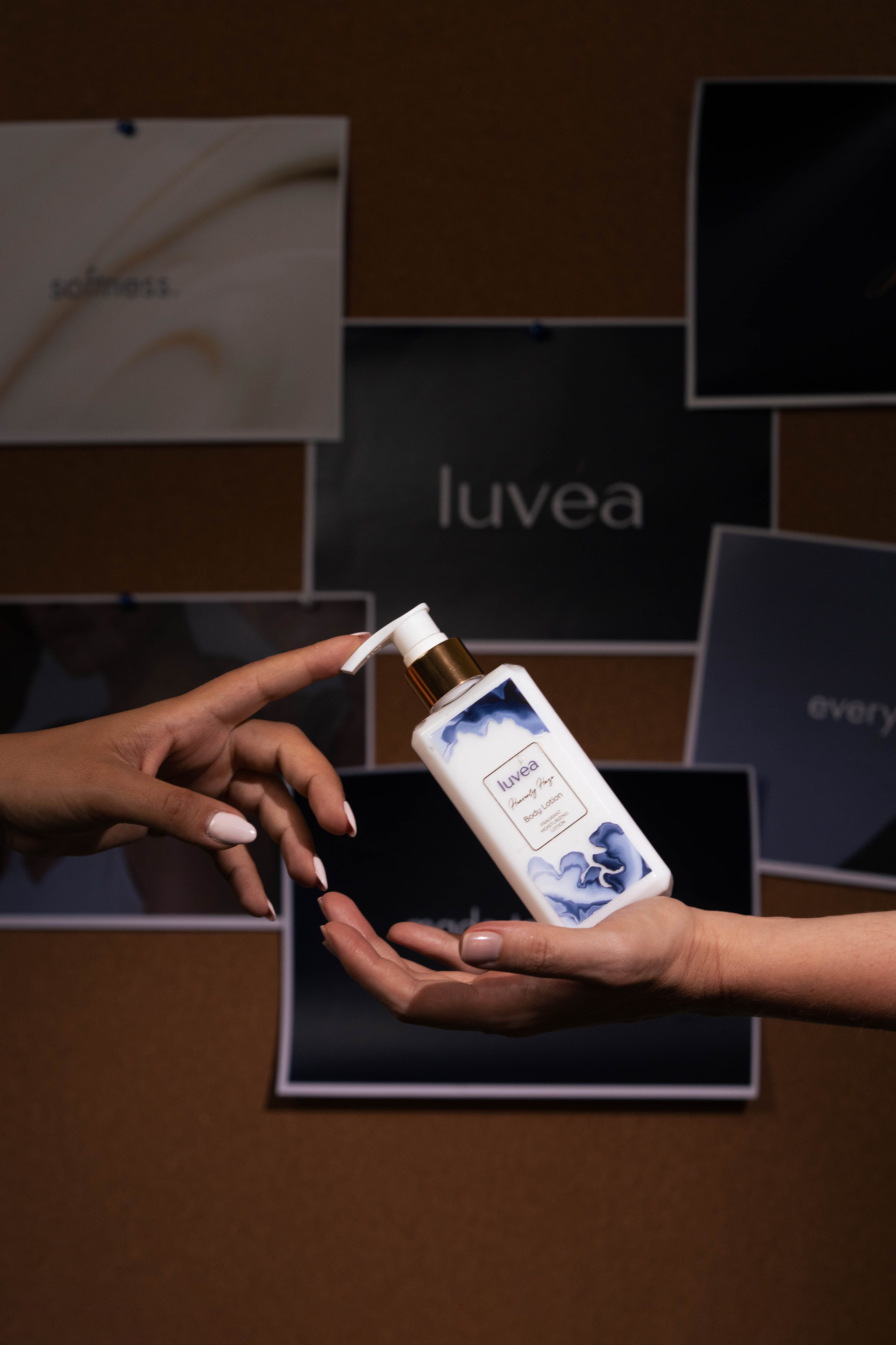 Two hands passing a Heavenly Haze lotion bottle against a dark editorial moodboard backdrop