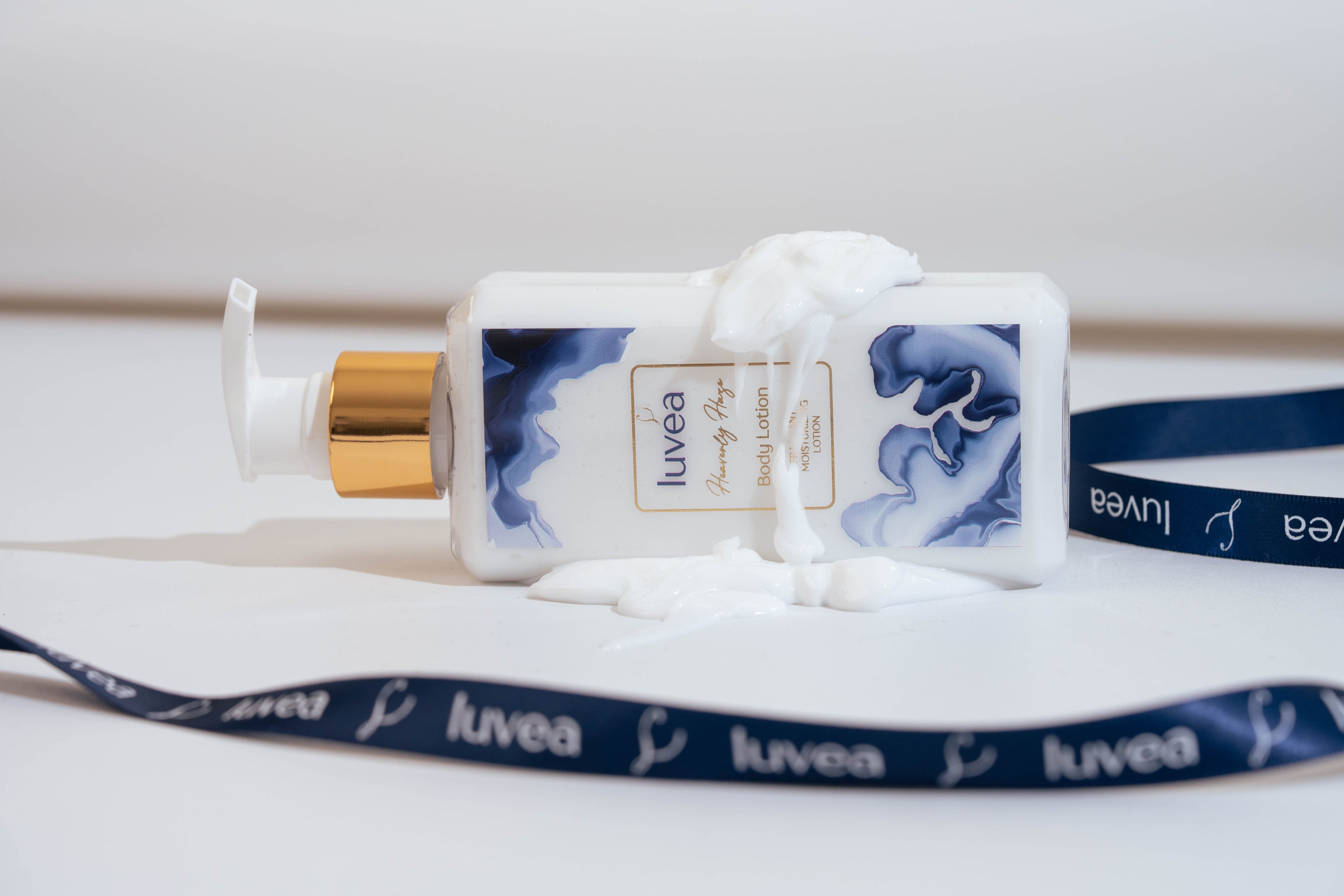 Heavenly Haze lotion bottle resting beside swirls of cream texture and a navy luvéa ribbon